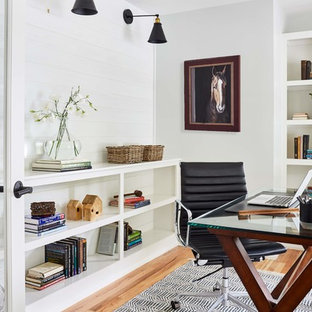 Foto på ett mellanstort lantligt hemmabibliotek, med vita väggar, ett fristående skrivbord, brunt golv och ljust trägolv