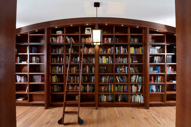 Diseño de despacho tradicional renovado con biblioteca, paredes blancas, suelo de madera clara, escritorio empotrado y suelo beige