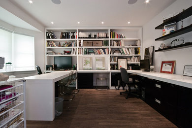 Diseño de despacho contemporáneo grande con paredes blancas, suelo de madera oscura y escritorio empotrado