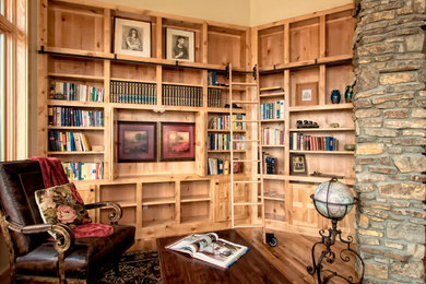Mid-sized mountain style medium tone wood floor and brown floor home office library photo in Denver with beige walls, a standard fireplace and a stone fireplace