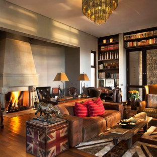 This is an example of a large bohemian home office in Other with medium hardwood flooring, a standard fireplace, a stone fireplace surround, brown floors and grey walls.