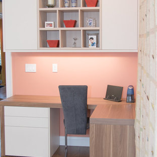 Modern inredning av ett mellanstort hemmabibliotek, med rosa väggar, mörkt trägolv och ett inbyggt skrivbord