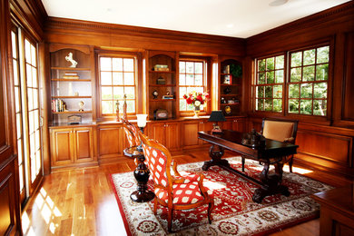 Imagen de despacho clásico grande con paredes marrones, suelo de madera en tonos medios y escritorio independiente