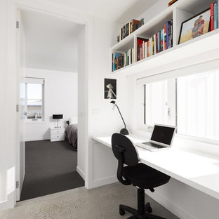 Minimalistisk inredning av ett hemmabibliotek, med vita väggar, betonggolv och ett fristående skrivbord
