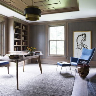 Bild på ett stort vintage hemmabibliotek, med bruna väggar, mörkt trägolv, en standard öppen spis, en spiselkrans i sten och ett fristående skrivbord
