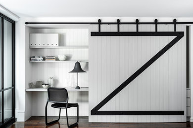 シドニーにあるインダストリアルスタイルのおしゃれな書斎 (白い壁、濃色無垢フローリング、造り付け机、茶色い床、パネル壁) の写真