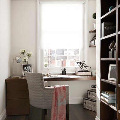 Trendy built-in desk dark wood floor home office photo in London with white walls