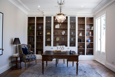 Modelo de despacho clásico con paredes beige, suelo de madera en tonos medios, escritorio independiente y suelo marrón