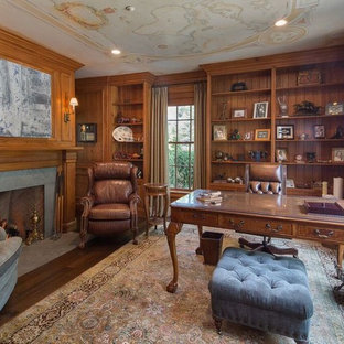 Mittelgroßes Klassisches Arbeitszimmer mit Arbeitsplatz, brauner Wandfarbe, dunklem Holzboden, Kamin, Kaminumrandung aus Beton, freistehendem Schreibtisch und braunem Boden in New York
