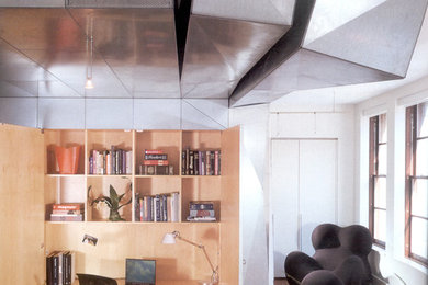 Imagen de despacho minimalista de tamaño medio sin chimenea con biblioteca, paredes beige, suelo de madera clara, escritorio empotrado y suelo marrón