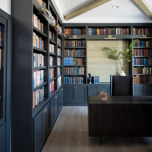 Klassisk inredning av ett mellanstort arbetsrum, med ett bibliotek, mörkt trägolv och ett fristående skrivbord
