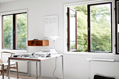 Minimalistisk inredning av ett arbetsrum, med vita väggar, ljust trägolv, ett fristående skrivbord och beiget golv