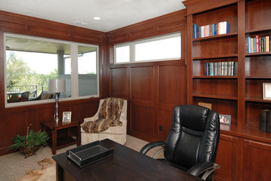 Klassisk inredning av ett mellanstort hemmabibliotek, med bruna väggar, heltäckningsmatta och ett fristående skrivbord