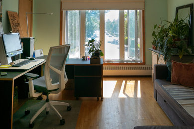Diseño de estudio bohemio de tamaño medio con paredes verdes, suelo de madera clara y escritorio independiente