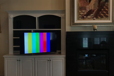 Modelo de cine en casa abierto actual de tamaño medio con paredes beige, suelo de madera en tonos medios, televisor colgado en la pared y suelo beige