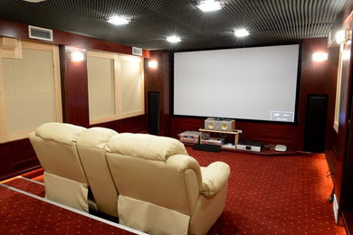 На фото: большой изолированный домашний кинотеатр в классическом стиле с коричневыми стенами, ковровым покрытием, проектором и красным полом