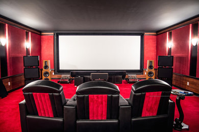 Cette image montre une grande salle de cinéma vintage fermée avec un mur rouge, moquette, un écran de projection et un sol rouge.