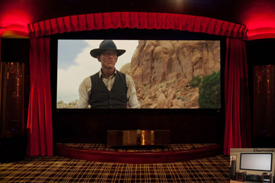 Modelo de cine en casa cerrado tradicional de tamaño medio con paredes negras, moqueta y pantalla de proyección