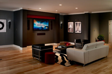 Foto de cine en casa abierto contemporáneo de tamaño medio con paredes grises, suelo de madera clara y televisor colgado en la pared