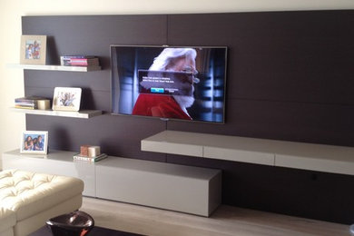 Modelo de cine en casa abierto minimalista de tamaño medio con paredes grises, suelo de madera clara y televisor colgado en la pared