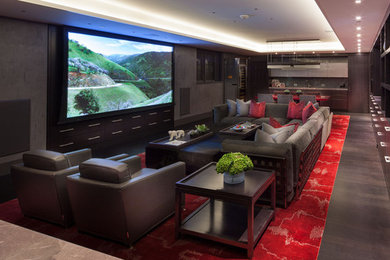 Aménagement d'une très grande salle de cinéma contemporaine ouverte avec un mur gris, parquet foncé, un écran de projection et un sol rouge.