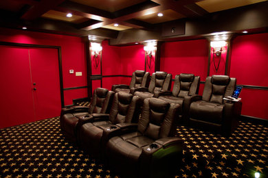 Modelo de cine en casa cerrado tradicional renovado de tamaño medio con paredes rojas, moqueta, pantalla de proyección y suelo negro