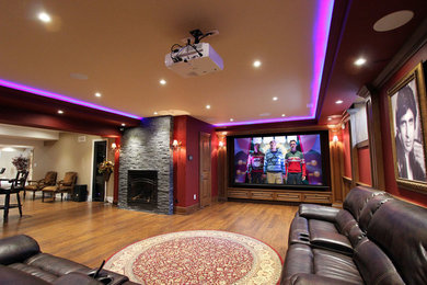 Diseño de cine en casa abierto clásico grande con paredes rojas, suelo de madera en tonos medios, pantalla de proyección y suelo marrón
