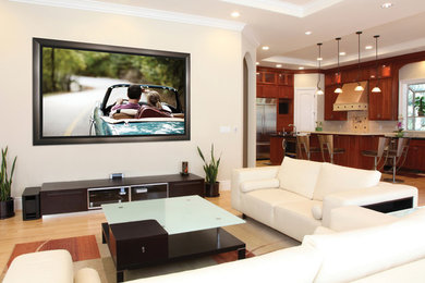 Modelo de cine en casa abierto contemporáneo grande con paredes beige, suelo de madera clara y televisor colgado en la pared