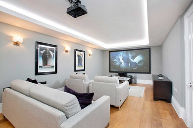 Ejemplo de cine en casa cerrado de tamaño medio con paredes grises, suelo de madera pintada, televisor colgado en la pared y suelo marrón
