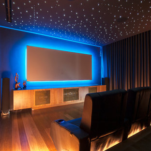Contemporary enclosed home theatre in Sydney with grey walls, medium hardwood floors, a wall-mounted tv and white floor.