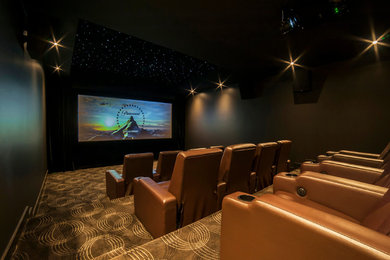 Cette photo montre une grande salle de cinéma tendance fermée avec un mur noir, moquette, un écran de projection et un sol multicolore.