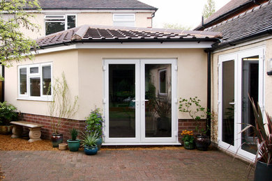 Idées déco pour une façade de maison beige moderne en stuc de taille moyenne et de plain-pied avec un toit à quatre pans.