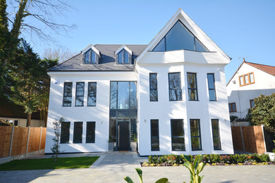 This is an example of a large and white modern render detached house in Essex with three floors, a pitched roof and a tiled roof.