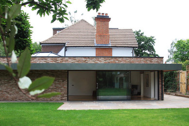 This is an example of a medium sized and multi-coloured contemporary brick house exterior in Surrey with three floors and a flat roof.