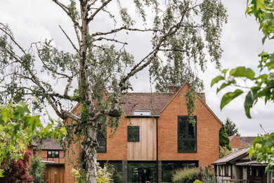 Foto de fachada de casa naranja actual de tamaño medio de dos plantas con revestimiento de ladrillo, tejado a dos aguas y tejado de teja de barro