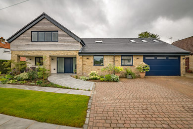 This is an example of a brown contemporary two floor detached house with a pitched roof, stone cladding and a grey roof.