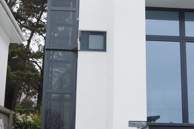 This is an example of a medium sized and white contemporary glass detached house in Dorset with three floors, a flat roof and a metal roof.