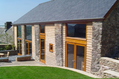 This is an example of a large and brown contemporary two floor house exterior in Devon with wood cladding and a pitched roof.