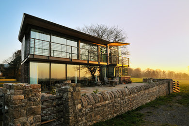 Contemporary two floor glass house exterior in Other with a lean-to roof.