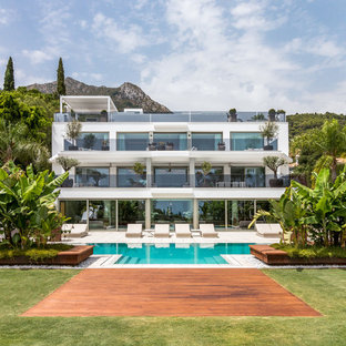 Modelo de fachada de casa blanca, actual, grande, de tres plantas, con tejado plano y revestimientos combinados