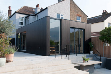 Photo of a medium sized and black contemporary bungalow semi-detached house in London with wood cladding, a flat roof and a mixed material roof.