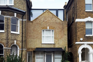 Photo of a medium sized and yellow contemporary brick semi-detached house in London with three floors, a flat roof and a metal roof.