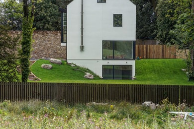 На фото: большой, трехэтажный, белый частный загородный дом в современном стиле с облицовкой из цементной штукатурки, двускатной крышей и черепичной крышей с
