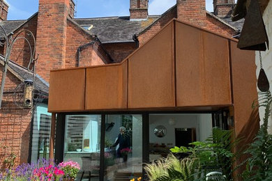 This is an example of a small and brown contemporary bungalow terraced house in West Midlands with metal cladding, a pitched roof and a mixed material roof.