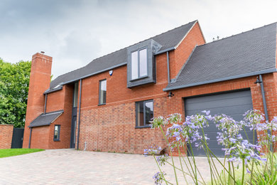 This is an example of a medium sized and red contemporary two floor brick detached house in Other with a pitched roof and a tiled roof.