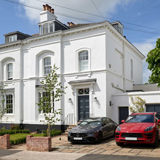 Cette image montre une façade de maison double blanche traditionnelle de taille moyenne et à trois étages et plus avec un revêtement en stuc, un toit à quatre pans et un toit en tuile.