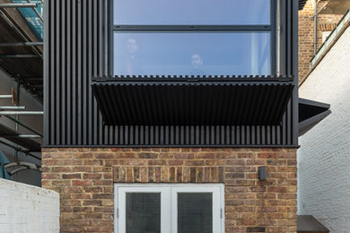 Photo of a small and black contemporary terraced house in London with three floors, wood cladding, a flat roof and a green roof.