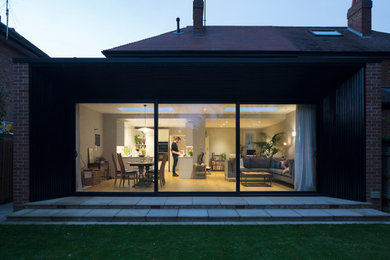 Photo of a medium sized and black modern two floor semi-detached house in Cambridgeshire with wood cladding, a flat roof and a metal roof.