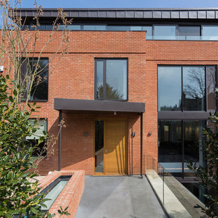 This is an example of a large and red contemporary brick detached house in London with three floors and a flat roof.