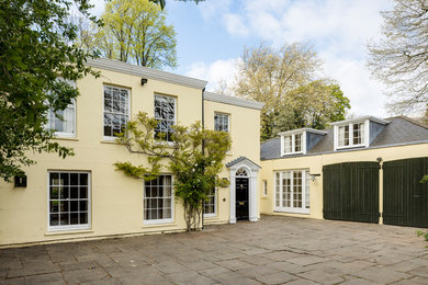 Large and yellow traditional two floor detached house in London with a flat roof.